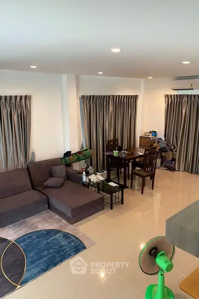 Spacious living room with modern furniture and dining area, featuring elegant curtains and tiled flooring.
