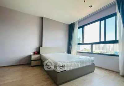 Spacious bedroom with large window offering city views, featuring modern furnishings and ample natural light.
