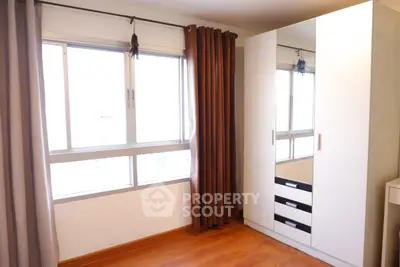 Bright bedroom with large window and modern wardrobe, featuring elegant curtains and wooden flooring.
