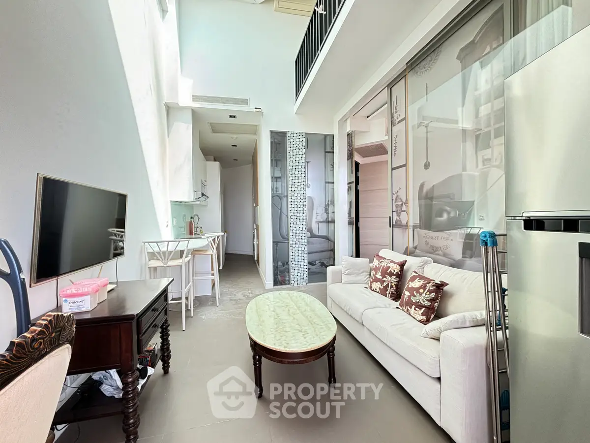Modern living room with high ceiling and mezzanine, featuring elegant furniture and open kitchen layout.