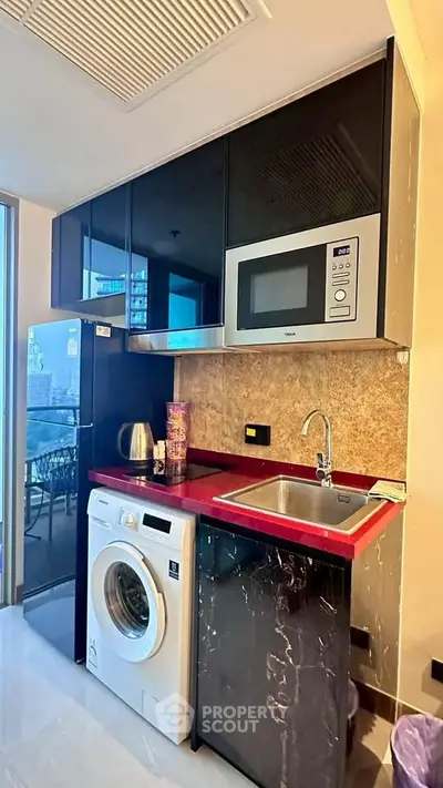Modern kitchen with sleek black cabinets, red countertop, and built-in appliances including microwave and washing machine.