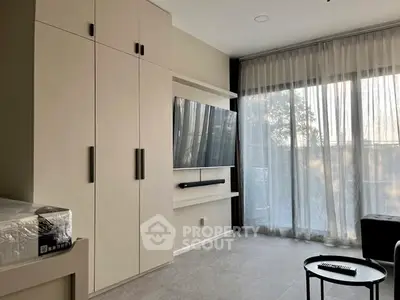 Modern living room with large TV and floor-to-ceiling windows for natural light.
