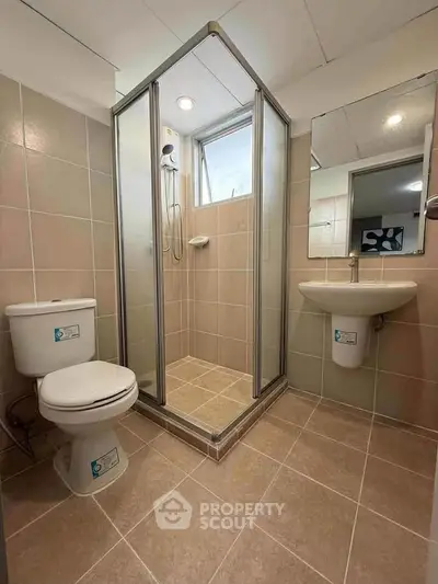 Modern bathroom with glass shower, toilet, and sink in a tiled setting.