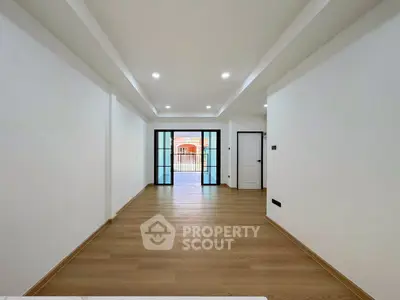 Spacious modern living room with wooden flooring and large glass doors leading to balcony.