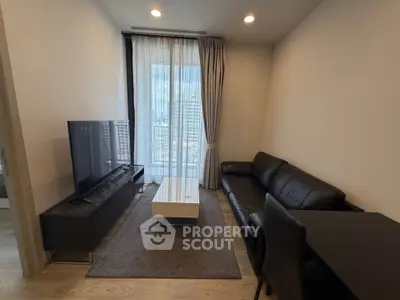 Modern living room with sleek black leather sofa and large TV, featuring floor-to-ceiling windows.
