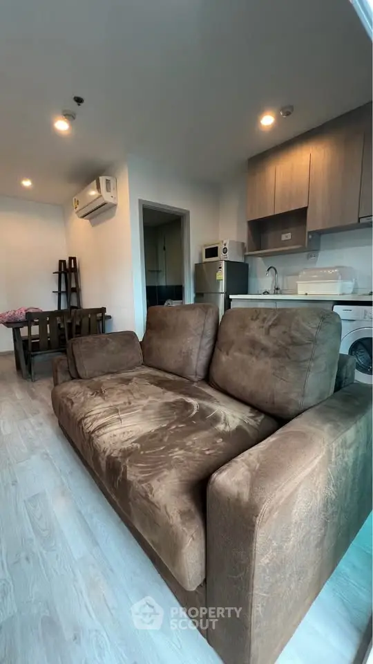 Cozy living room with plush brown sofa and modern kitchen in open layout apartment.