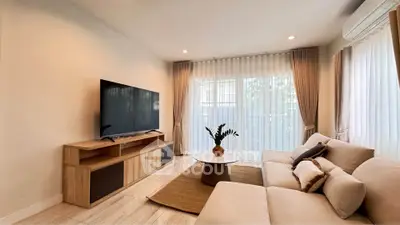 Modern living room with large TV, cozy sofa, and elegant decor in a bright, airy space.