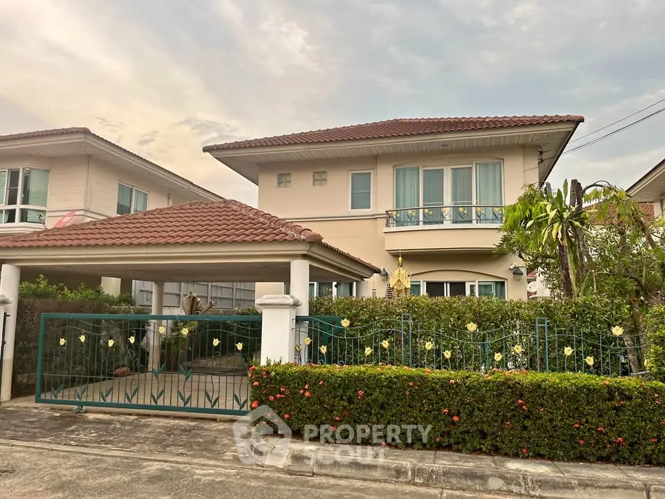 Charming suburban house with tiled roof and gated driveway, surrounded by lush greenery and a well-maintained garden.