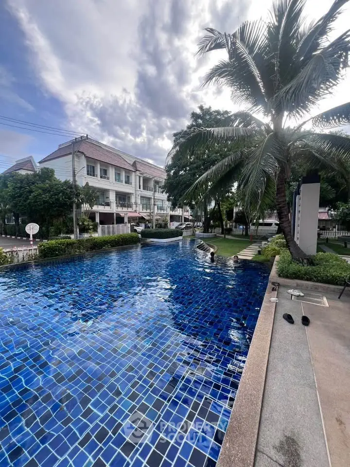 Luxurious residential pool with palm trees and elegant townhouses in the background, perfect for relaxation.