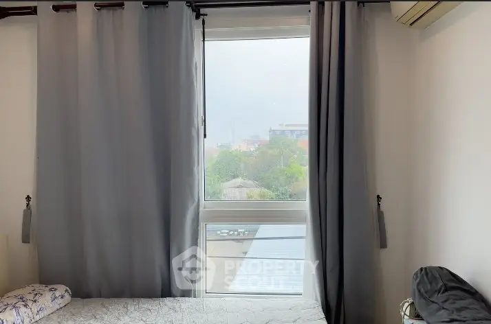 Cozy bedroom with large window and gray curtains offering a serene view.