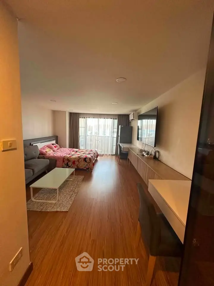 Spacious living room with modern decor and large TV, featuring a cozy seating area and stylish wooden flooring.