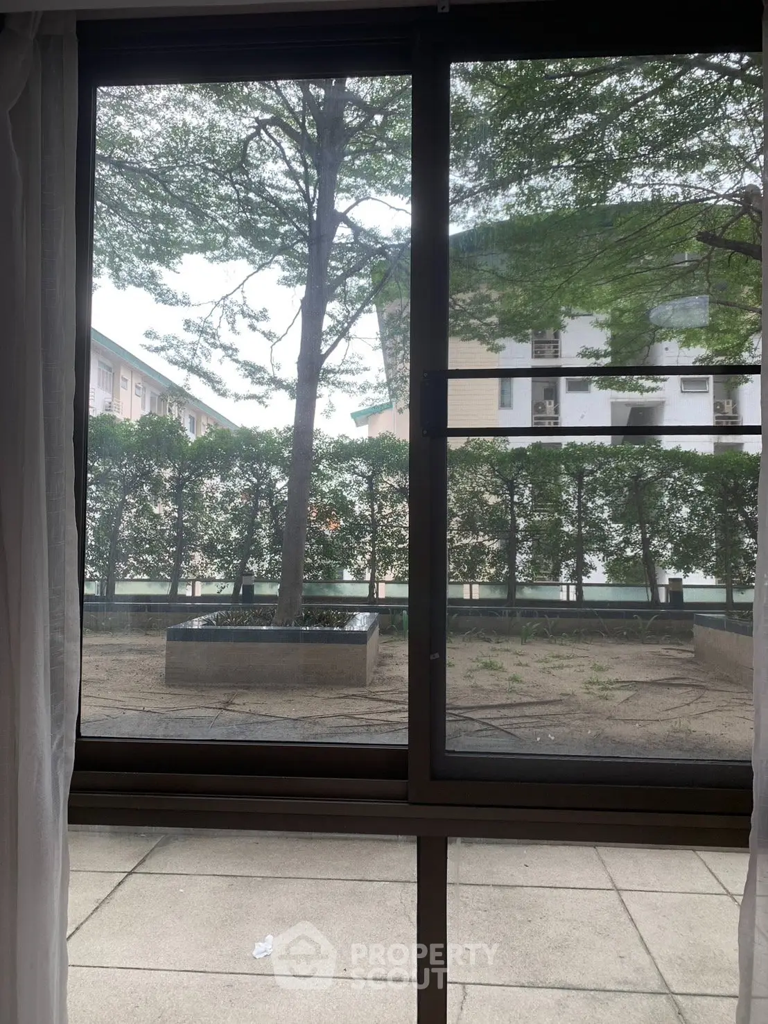 Serene view from window overlooking lush greenery and modern buildings, perfect for urban living.