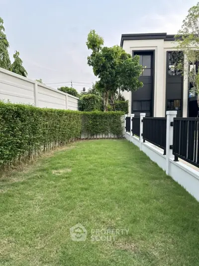 Spacious garden area beside modern building with lush greenery and privacy fence.