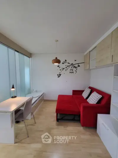 Modern living room with red sofa, stylish decor, and workspace in a bright apartment.