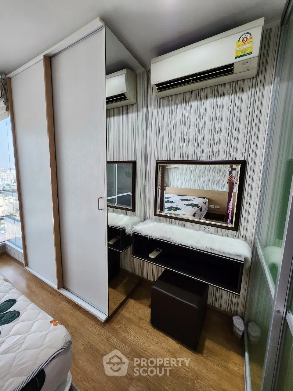 Modern bedroom with stylish wardrobe and vanity area, featuring air conditioning and wooden flooring.