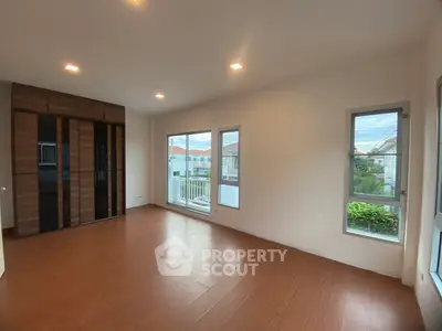 Spacious bedroom with wooden flooring and large windows offering natural light.