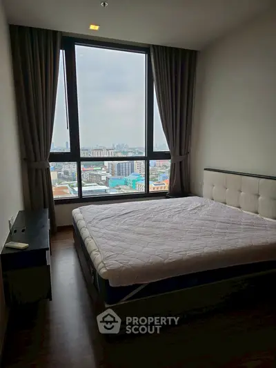 Spacious bedroom with large window offering stunning city views in modern apartment.