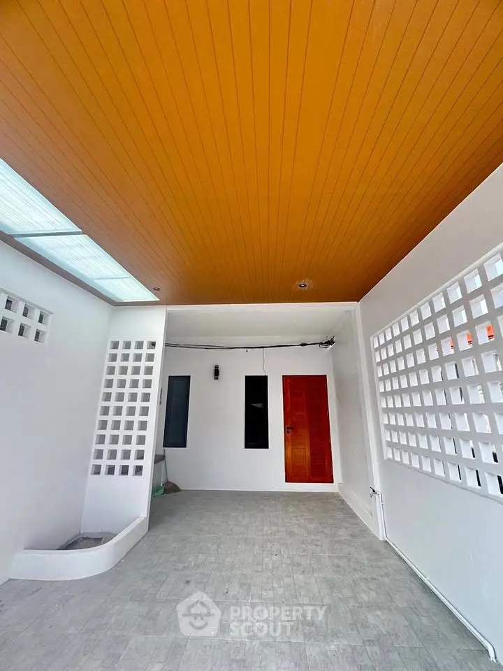 Modern covered entrance with wooden ceiling and stylish red door