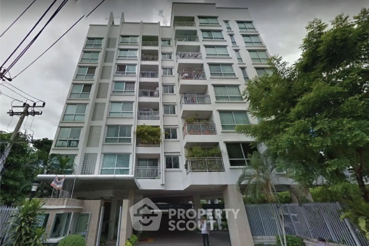 Modern multi-story residential building with lush greenery and gated entrance.