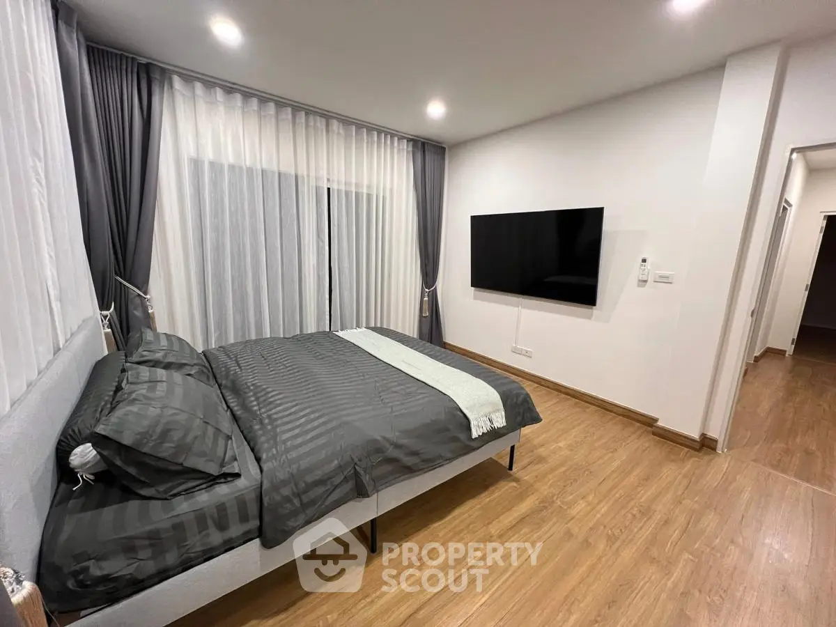 Modern bedroom with sleek design and wall-mounted TV, featuring elegant curtains and wooden flooring.