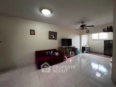 Spacious living room with tiled flooring and ceiling fan, featuring a cozy sofa and entertainment center.