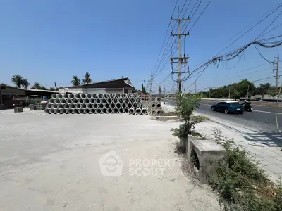Spacious roadside plot with stacked concrete pipes, ideal for commercial development.
