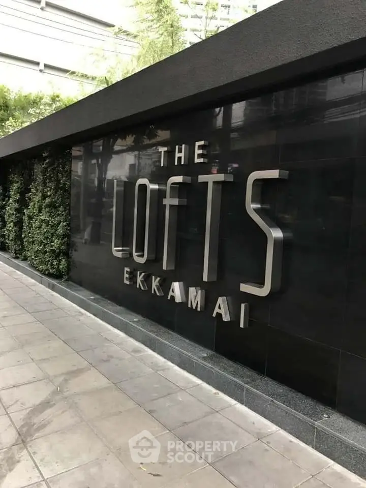 Modern exterior of The Lofts Ekkamai with sleek signage and lush greenery.