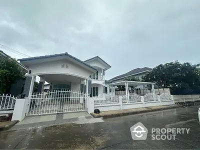 Elegant two-story white house with gated driveway and lush greenery on a rainy day.