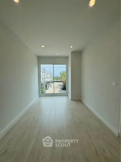 Spacious empty room with large window and wooden flooring, perfect for customization.