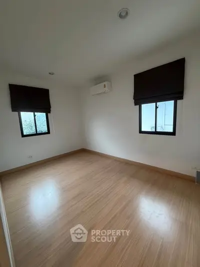 Spacious empty bedroom with wooden flooring and air conditioning, ready for customization.