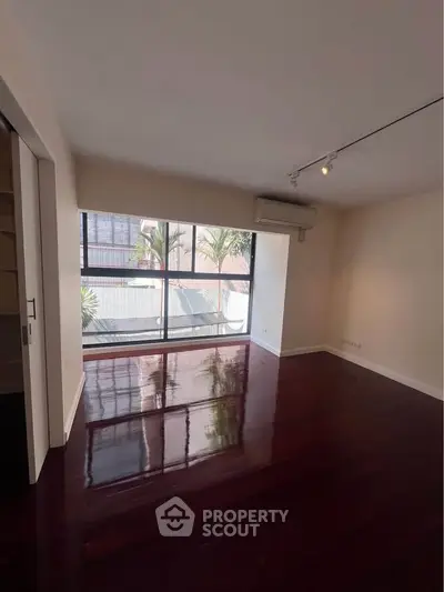 Spacious empty room with polished wooden floors and large window offering natural light.