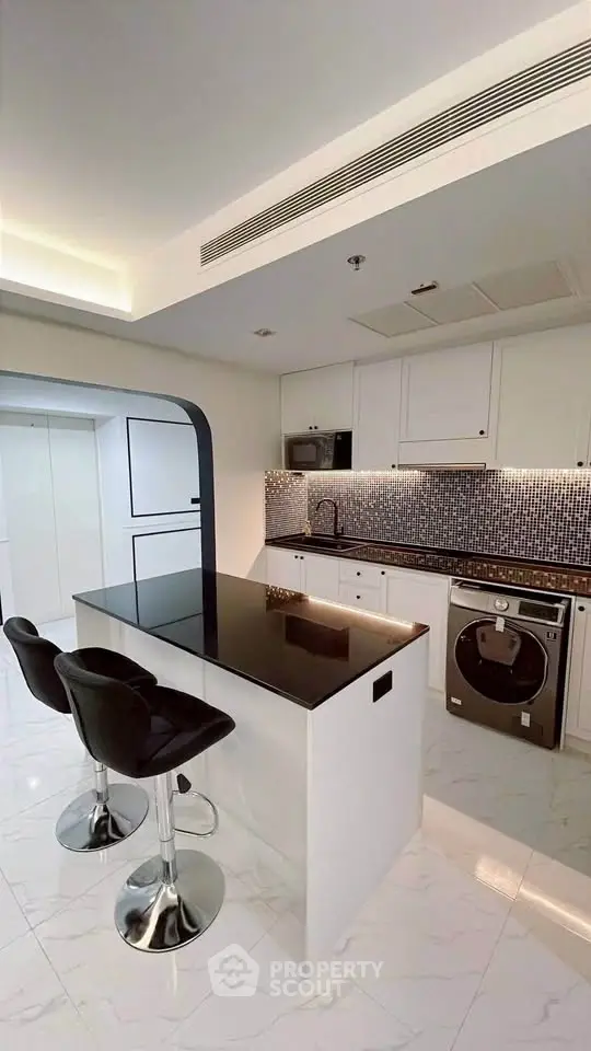 Modern kitchen with sleek black countertop and built-in appliances, featuring stylish bar stools and elegant lighting.