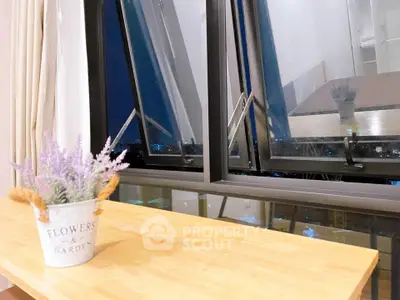 Charming interior view with open window and cityscape, featuring a decorative flower pot on a wooden table.