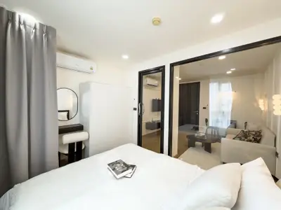 Modern bedroom with stylish decor and view into a cozy living room, featuring elegant furniture and ambient lighting.