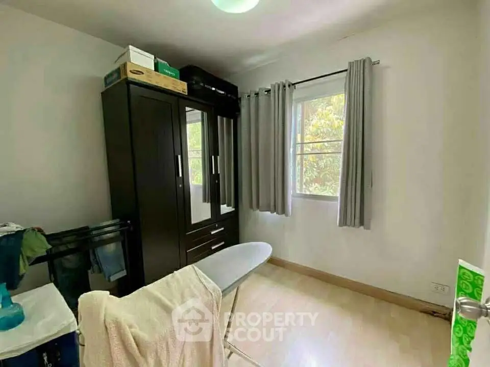 Cozy bedroom with wardrobe and ironing board, natural light from window, ideal for compact living.