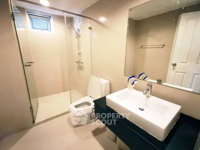 Modern bathroom with glass shower and sleek fixtures in contemporary home.