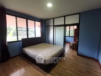 Spacious bedroom with large windows and wooden flooring in modern apartment.