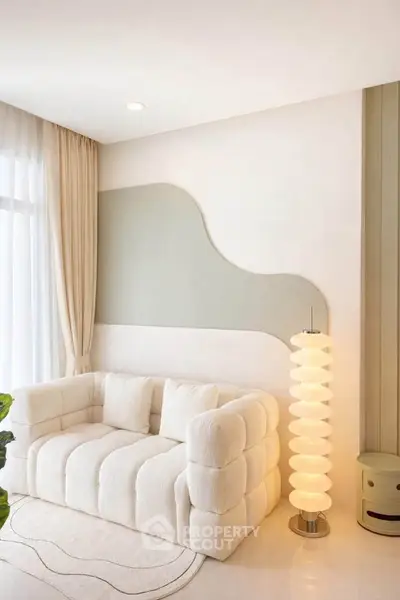 Elegant living room with plush white sofa and modern floor lamp, featuring stylish wall decor and natural light.