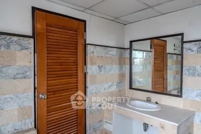 Spacious bathroom with elegant marble tiles and wooden door, featuring a modern sink and large mirror.