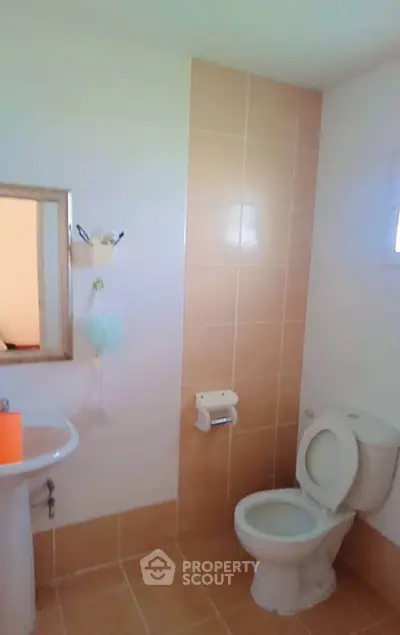 Modern bathroom with beige tiles and white fixtures, featuring a sink and toilet.