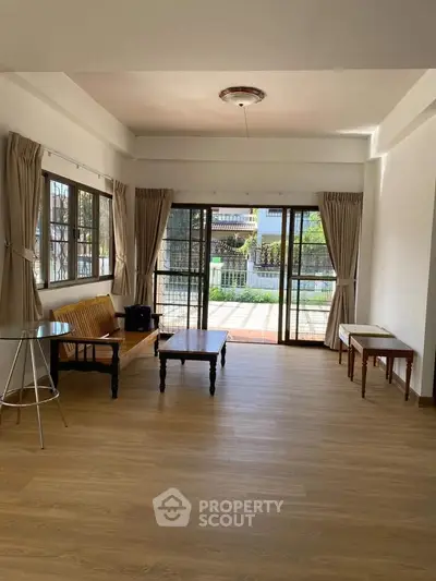 Spacious living room with wooden flooring and large windows offering natural light and garden view.