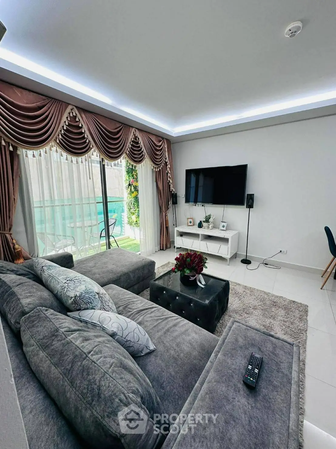 Luxurious living room with elegant drapes, plush gray sofa, and large TV, overlooking a serene pool view.