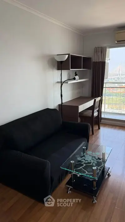 Modern living room with black sofa, glass coffee table, and study desk with city view.