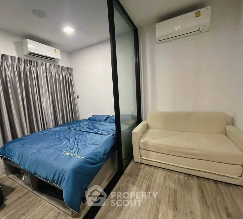 Modern bedroom with glass partition and cozy sofa, featuring air conditioning and stylish flooring.