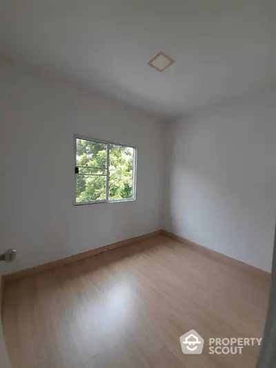 Bright and airy bedroom with large window offering a serene tree-lined view, featuring gleaming hardwood floors and a fresh, neutral color palette.