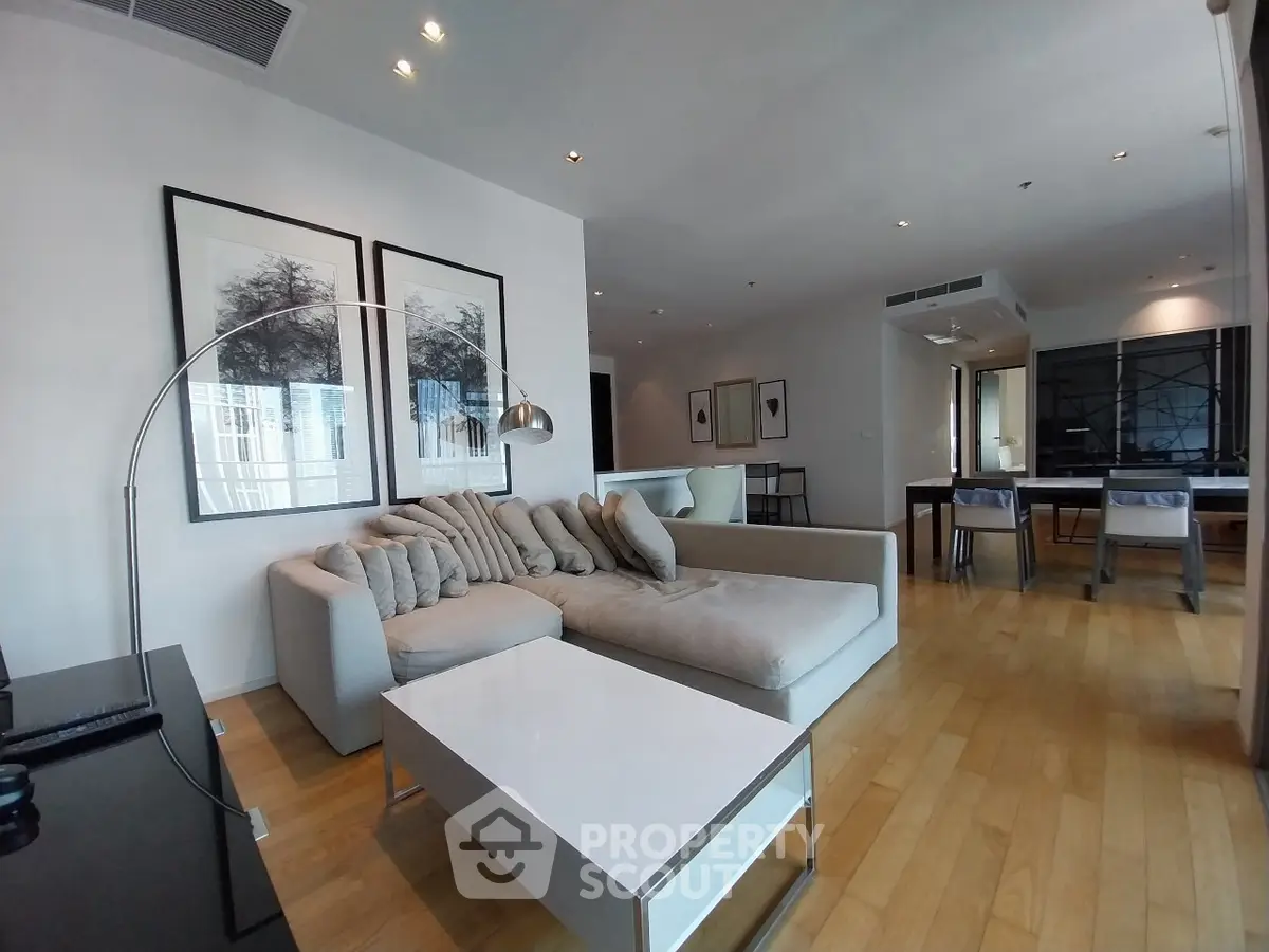 Spacious modern living room with elegant decor and open dining area, featuring hardwood floors and stylish furnishings.