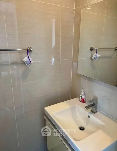 Modern bathroom with sleek sink and mirror, featuring neutral tile design.