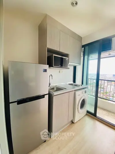Modern kitchen with balcony view, featuring fridge, microwave, and washing machine in a compact layout.