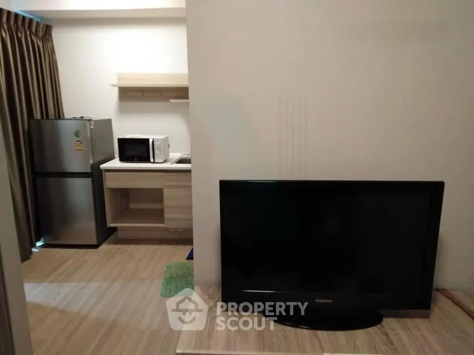 Modern studio apartment with compact kitchen and living area featuring a TV and fridge.