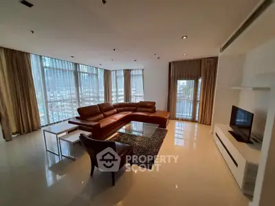 Spacious modern living room with city view, featuring elegant leather furniture and large windows.